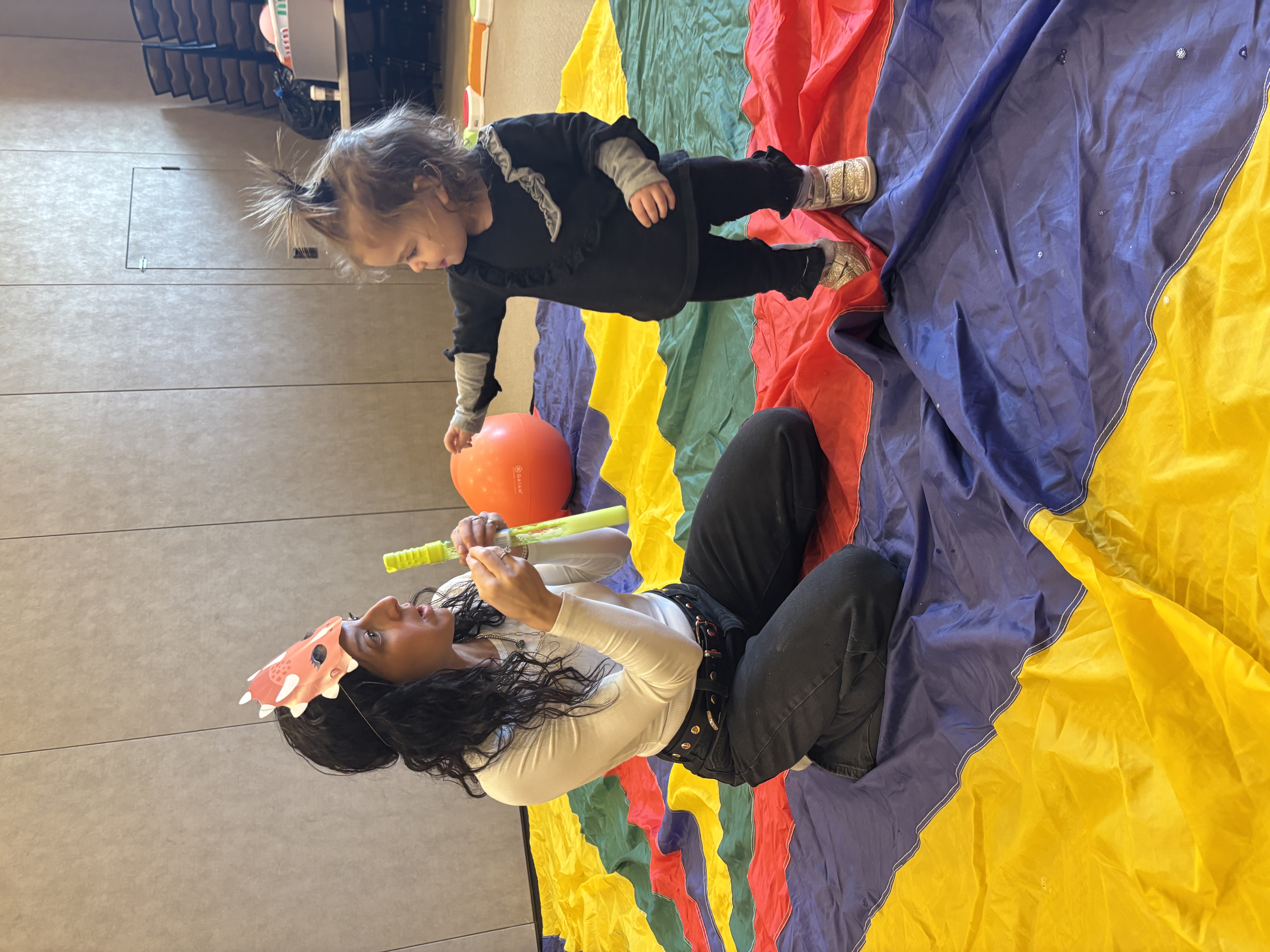 Rebeca leading a playful occupational therapy session with a young child on a colorful parachute