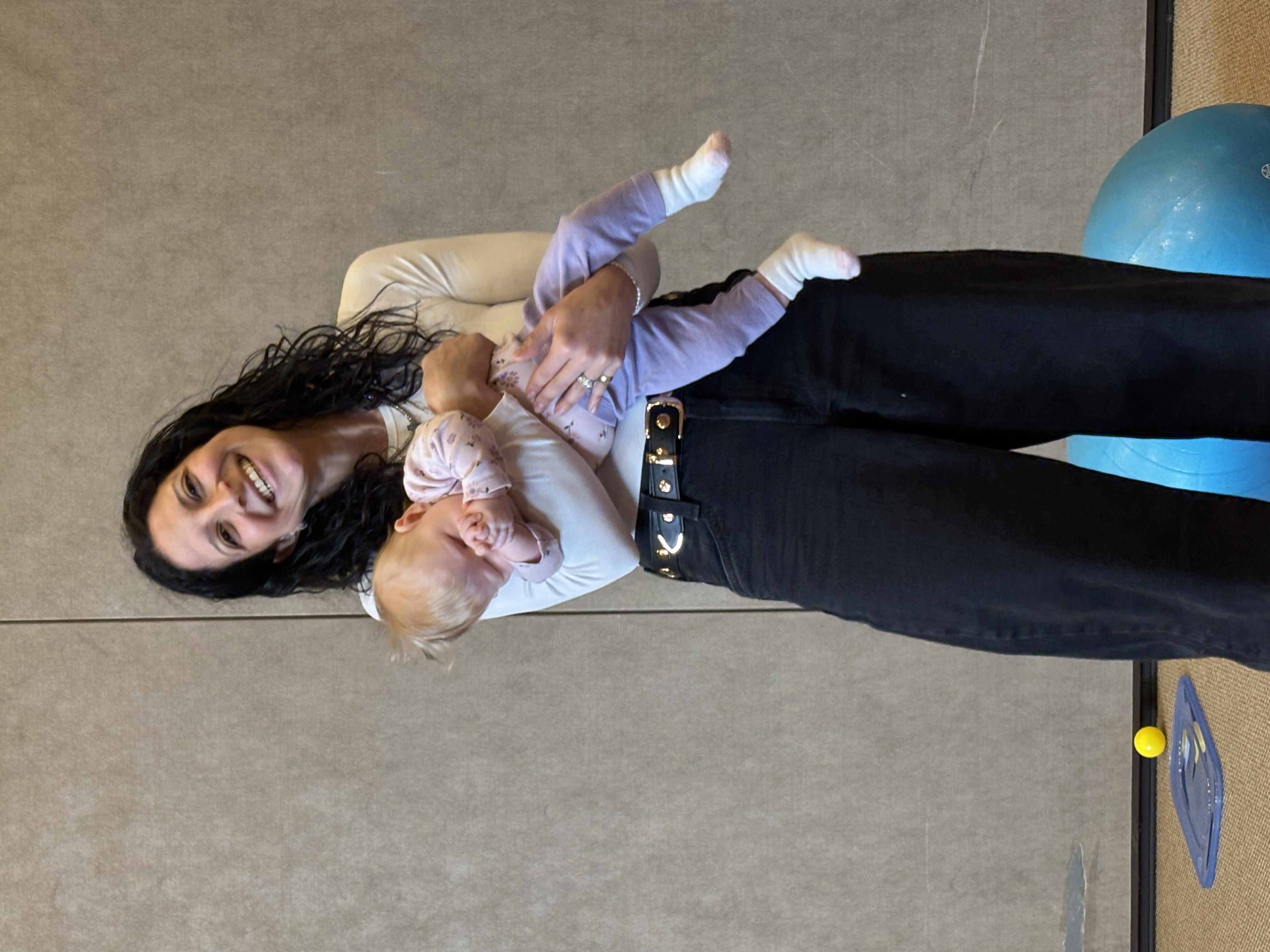 Rebeca, pediatric occupational therapist, smiling warmly while holding a baby during a therapy session